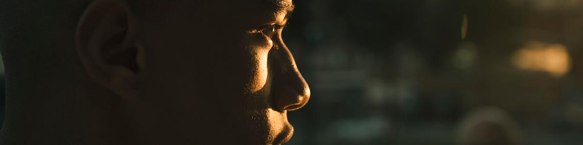 Portrait de profil d'un homme baigné dans la lumière dorée d'une fin de journée. L'arrière plan est flou mais laisse deviner la ville de Marseille. 